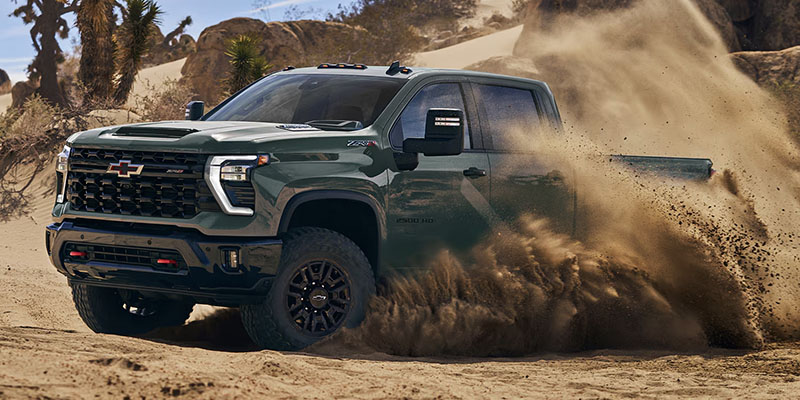 A black 2026 Chevrolet Silverado 2500 skidding up a sandstorm in an empty desert plot of land.