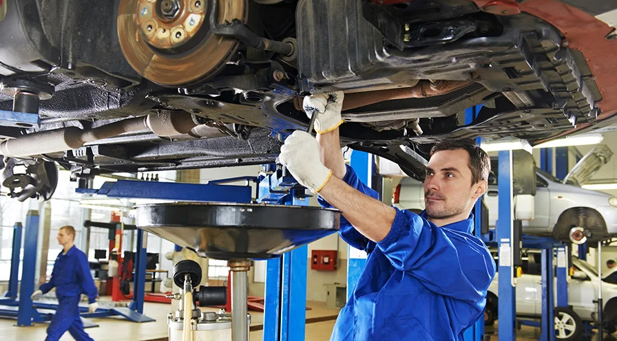 Certified professional mechanics wearing bright blue work outfits work on the underside of raised cars in the GMC Chevrolet Service Center